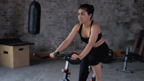 A beautiful athletic young brunette woman in sportswear trains on a sycle in the gym