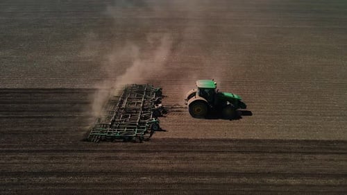 Tractor with harrow system plowing ground on cultivated farm field, agriculture.