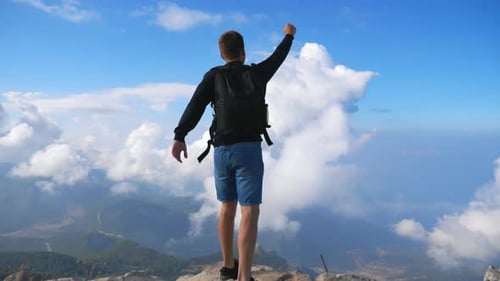 Hiker with Backpack Standing on Mountain Edge and Victoriously Raising His Hand. Man Actively