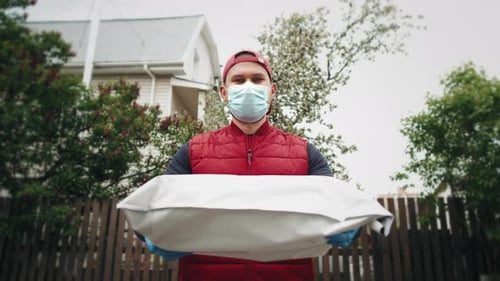 Delivery Concept Portrait of Happy Spanish Delivery Man with Face Mask in Red Cloth Holding a Box