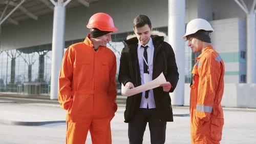 Investor des Projekts im schwarzen Anzug bei der Untersuchung des Bauobjekts mit Bauarbeitern in