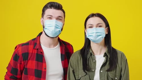 Young Couple Smiling Wearing Face Masks on Yellow