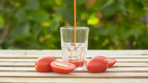 Pouring red tomato juice into a glass with vegetables on wooden table