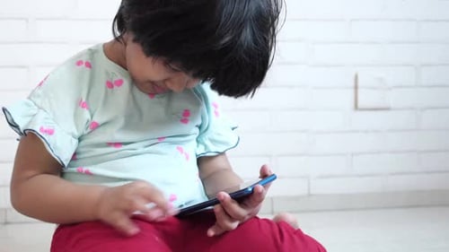 Child Plays with a Smartphone in Front of Wall