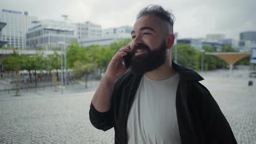 Smiling Bearded Man Strolling on Street While Talking on Phone