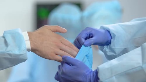 Krankenschwester hilft dem Arzt, medizinische Handschuhe vor der Operation anzuziehen, Sterilität im Krankenhaus