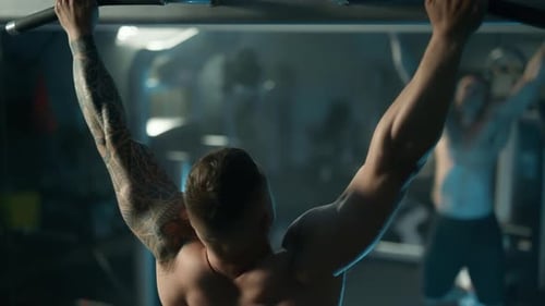 A Handsome Young Muscular Sportsman is Doing Exercise on a Fitness Machine in the Gym