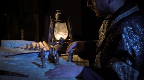 Man Moves Chess Pieces Across Map Under Lantern Light