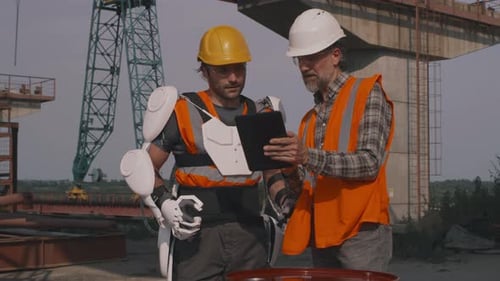 Construction Workers Using Tablet with Exoskeleton on Site