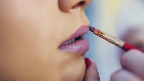 Nahaufnahme eines professionellen Visagisten, der Lippenstift auf die Lippen eines Models aufträgt und in der Schönheitspflege arbeitet