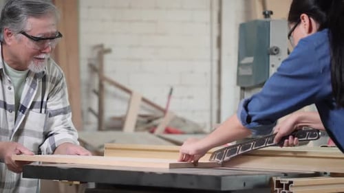 Woman Cuts Wood with Man Supervising in Workshop