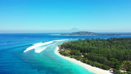 Big white waves splashing on white sandy beach of tropical island with lush vegetation surrounded by