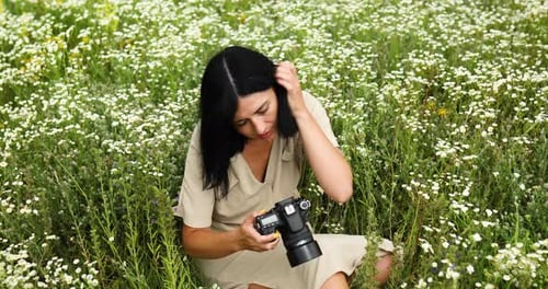 Female photographer sitting on flower field landscape and looking photo on camera