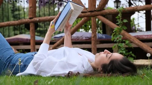 Young Girl Reading Book Lying on Green Grass