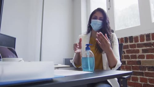Woman wearing face mask sanitizing her hands at office