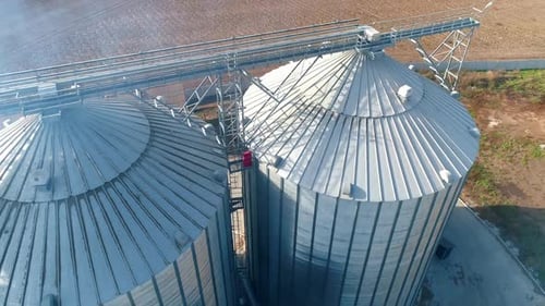 Metal silos on field. Large containers for storing and processing grains. Silver grain elevators