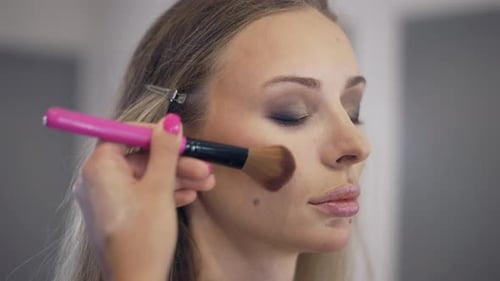 The Makeup Artist Applies the Powder on the Surface of the Young Blonde's Face