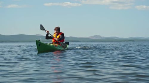 Man Paddles Kayak in Lake on Sunny Day