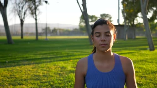A beautiful young woman yogi sitting on a yoga mat in peaceful meditation in the park at sunrise.