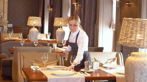 Mujer joven arregla cubiertos en una mesa en un restaurante
