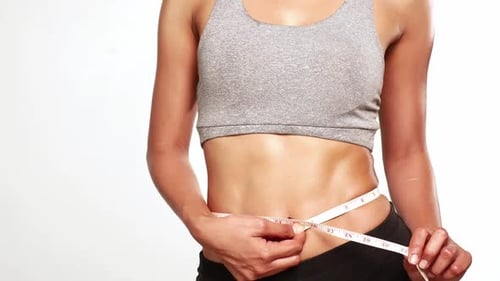 Slim perfect female body in sportswear measuring waist with measure tape on white background