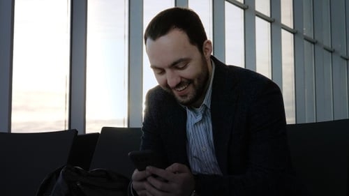 Young Man Smiling, Looking at Phone Indoors