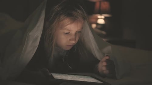 Teenager-Mädchen im Bett spielt im dunklen Licht ein Tablet im sozialen Internet. Nahaufnahme von Little Girl