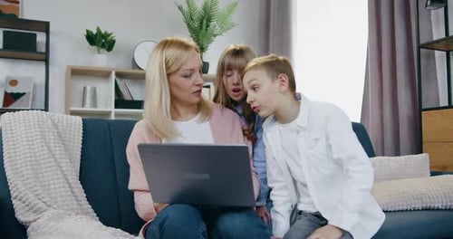 Madre revisando un interesante Vídeo en una computadora portátil junto con su sonriente y amistoso hijo y su hija