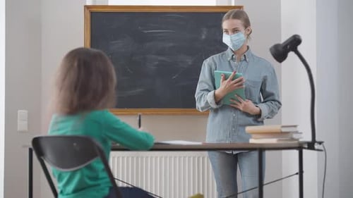 Teacher instructs student in classroom while wearing mask
