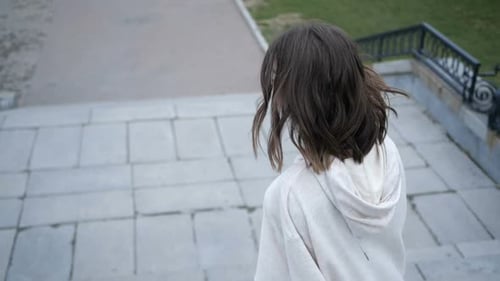 A Young Girl with Brown Hair Walks Around the City Going Down the Stairs