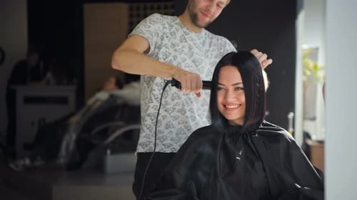 Stylist Straightening Woman's Hair in Modern Salon