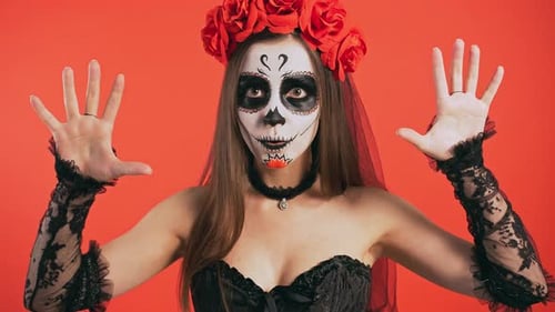 Mujer del Día de Muertos con maquillaje de calavera de azúcar que te asusta con las manos diciendo abucheo y sonriendo posando
