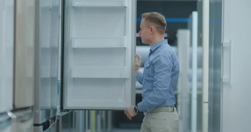 The Man Open the Door of the Refrigerator in the Appliances Store and Compare with Other Models To