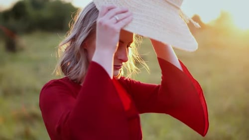 Woman Putting on Hat in Field at Sunset