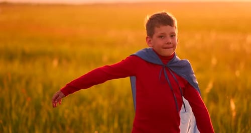 Boy Dressed as Superhero in Field at Sunset