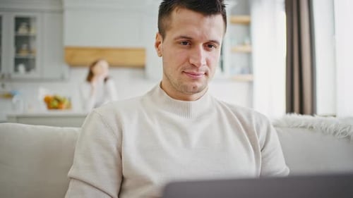Close Up Concentrated Selfisolated Man Working on Laptop at Home His Wife on Background