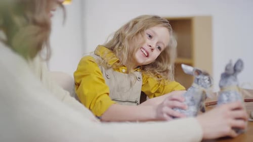 Smiling Girl with Bunny Figurines at Table