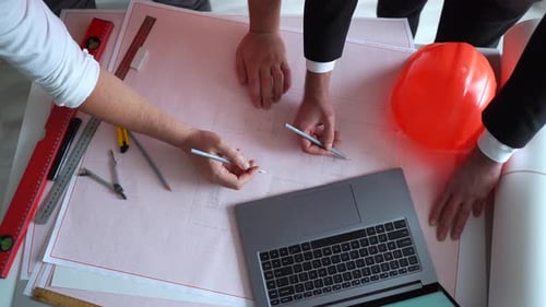 Top View of Workers Pointing to Building on Blueprint and Using Laptop
