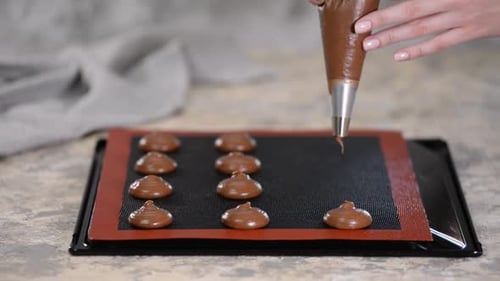 Hands Piping Chocolate Batter onto Baking Tray