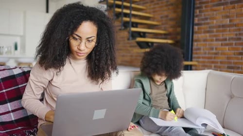 Woman Works on Laptop as Child Draws