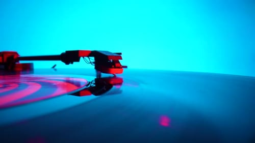 Black Vinyl Record Spinning and Play Music on Old Turntable in Rays of Bright Red and Blue Neon