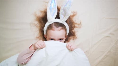 Girl with Bunny Ears Hides Behind Blanket in Bed