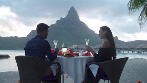 Man and woman couple toasting with champagne on beach, tropical island resort sunset, Bora Bora