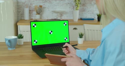 Young Woman at Home Works on a Laptop Computer with Green Mock-up Screen. Working at Home in