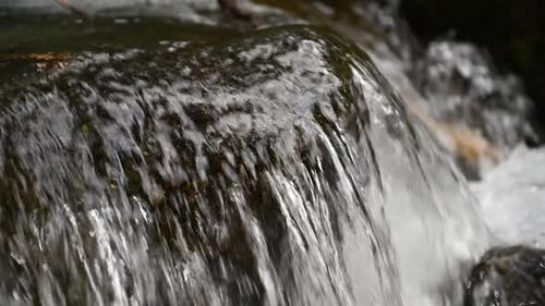 Slow motion of wild clear mountain river , stream flowing through rocks.