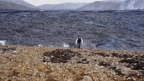 Photographer Walking As Smoke Rises From Lava Field Behind