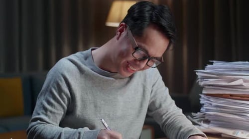 Close Up Of Smiling Asian Man Enjoys Working With Documents At Home