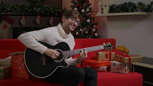 Man Plays Guitar at Christmas on Red Couch