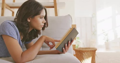 Woman Reads Book on Sofa and Smiles