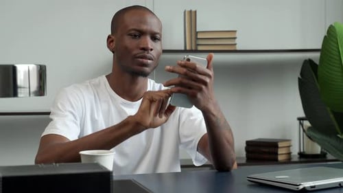 Black Man Uses a Smartphone While Sitting at a Desk in the Office